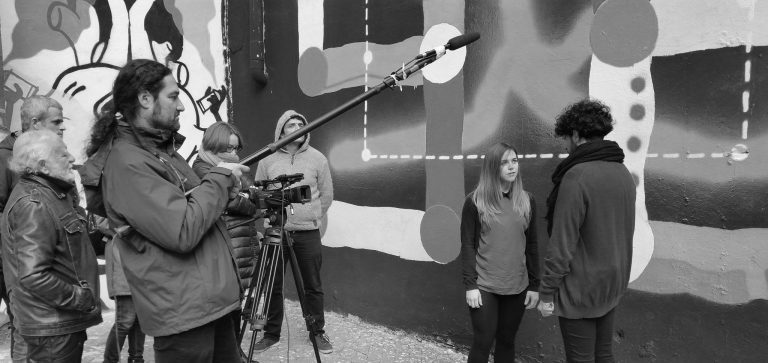 Directora de cine, equipo técnico y actores en un rodaje de cine en una calle con grafitis de fondo en invierno