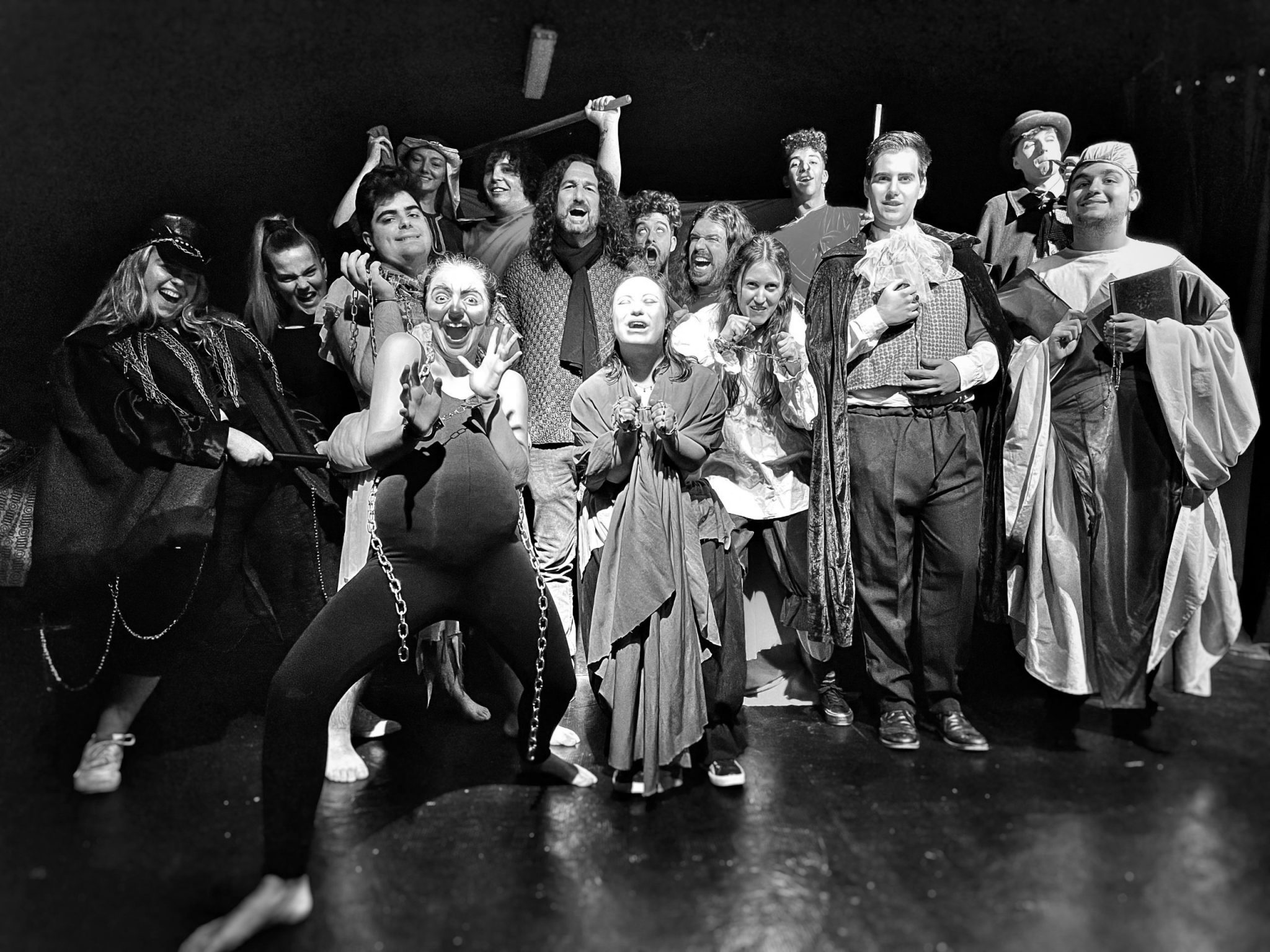 Grupo de actores y director en la sala de teatro iluminados por los focos con tonalidad cálida y caracterizados con los personajes