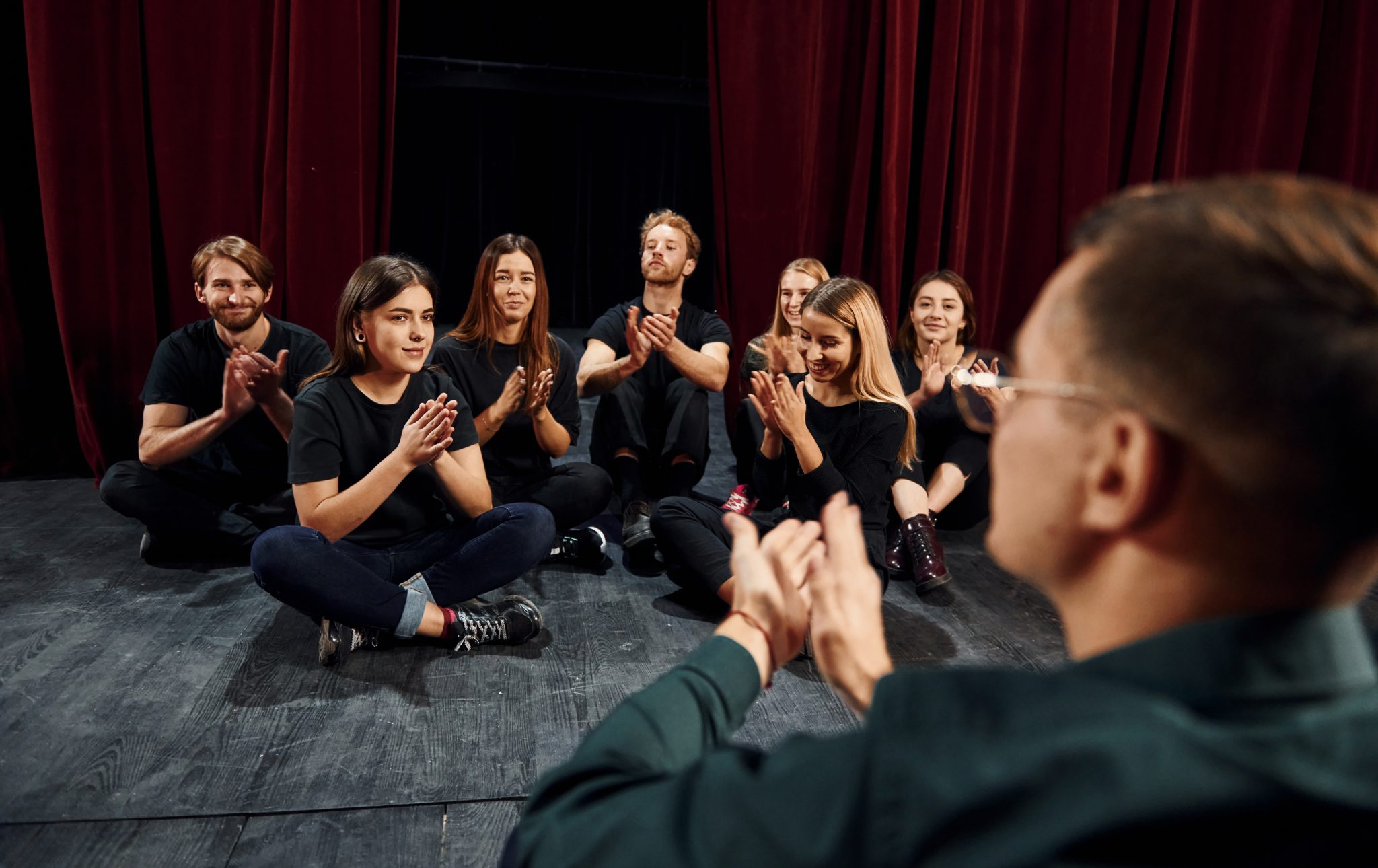 alumnos de teatro y profesor sentados en el suelo tocando palmas para el ritmo