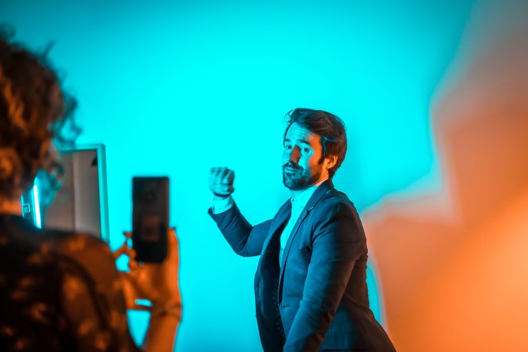 Un chico con traje de chaqueta posando con el brazo cerrando el puño como señal de lucha obrera, y una chica haciendo sosteniendo un móvil con ambas manos. Fondo azul claro.