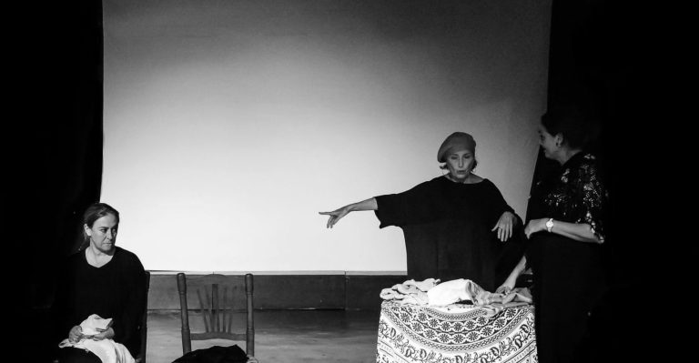 La majestuosa actriz Verónica Forqué dando indicaciones con su brazo a una de las actrices pero sin mirarla. Una de las actrices está de pie y la otra sentada.